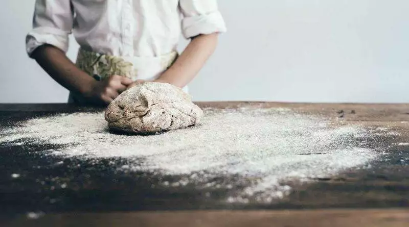 Ein Mädchen knetet Teig auf einem Holztisch, während es Brot backt.