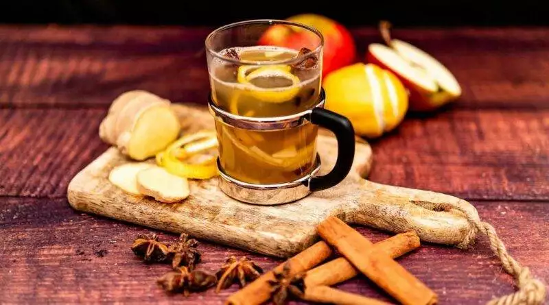 Eine Tasse Glühwein mit Zimtstangen und Äpfeln auf einem Holzbrett.