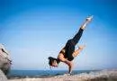 Eine Frau übt Yogaklassen, indem sie einen Handstand auf einem Felsen vor dem Meer macht.