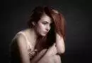 Eine Frau mit roten Haaren posiert vor dunklem Hintergrund.