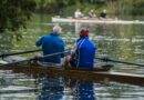Zwei Männer rudern in einem Ruderboot auf einem See.