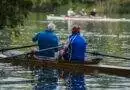 Zwei Männer rudern in einem Ruderboot auf einem See.