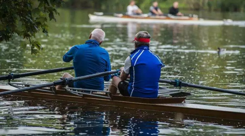 Zwei Männer rudern in einem Ruderboot auf einem See.