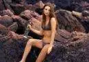 Eine Frau im Bikini sitzt mit einer Flasche Wasser auf Felsen.