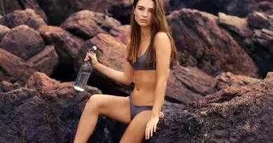 Eine Frau im Bikini sitzt mit einer Flasche Wasser auf Felsen.